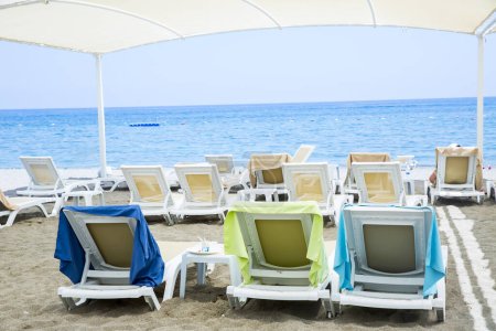 Téléchargez les photos : Chaises longues en plastique blanc sur la plage de sable sous grand parasol - en image libre de droit
