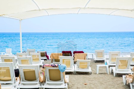 Téléchargez les photos : Chaises longues en plastique blanc sur la plage de sable sous grand parasol - en image libre de droit