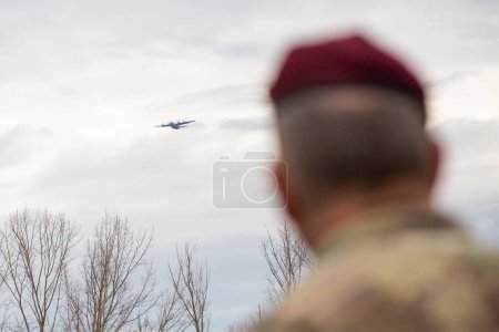 Téléchargez les photos : Retour recadré du soldat en uniforme de camouflage et casque regardant l'avion dans le ciel - en image libre de droit