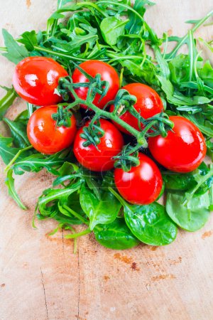 Foto de Tomates rojos frescos en la madera y las hojas de ensalada verde - Imagen libre de derechos