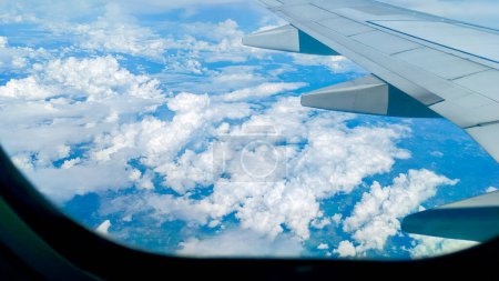Téléchargez les photos : Vue aérienne d'un ciel bleu clair magnifique avec des nuages duveteux vus à travers une fenêtre d'avion. Concept de voyage - en image libre de droit
