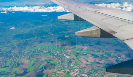 Téléchargez les photos : Vue aérienne panoramique regardant par une fenêtre d'avion vers le monde ci-dessous. Beau ciel bleu clair avec des nuages duveteux. Concept de voyage - en image libre de droit