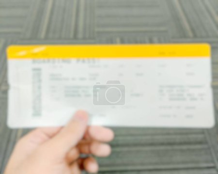 Téléchargez les photos : Voyageur tenant une carte d'embarquement avec un aéroport flou en arrière-plan. Concept de voyage - en image libre de droit