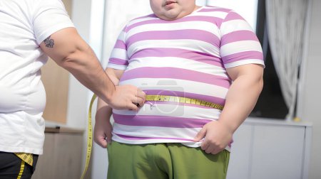 Téléchargez les photos : Obèse garçon mesure son gros ventre avec un ruban à mesurer à la clinique Générative AI - en image libre de droit