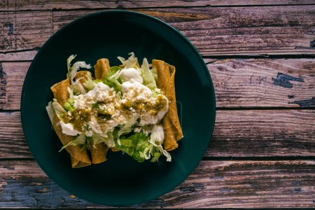 Photo for Tacos flauta with cheese, cream and lettuce on a wooden table. Mexican snacks. - Royalty Free Image