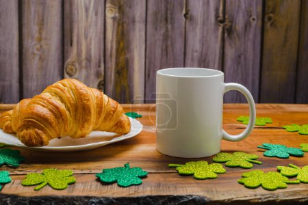 Photo for White cup and croissants on wooden table with glittering clovers. St. Patrick's Day mock-up. - Royalty Free Image