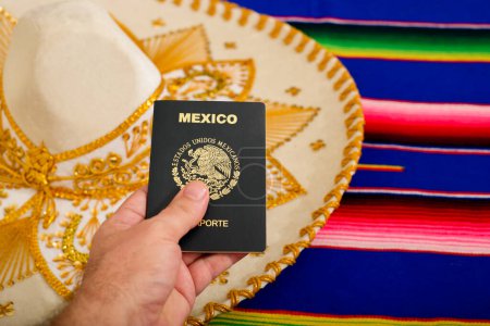 Photo for Man hand holding Mexican passport and mariachi hat on colorful serape. Concept of mexicanity. - Royalty Free Image