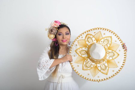 Photo for Mexican woman with flower headdress holding a mariachi hat. Woman with sombrero, white background. - Royalty Free Image