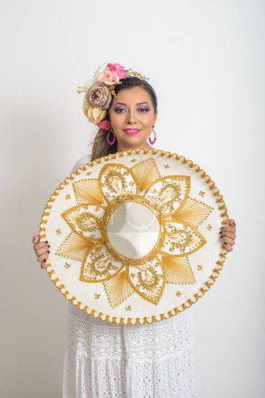 Photo for Mexican woman with flower headdress holding a mariachi hat. Woman with sombrero, white background. - Royalty Free Image