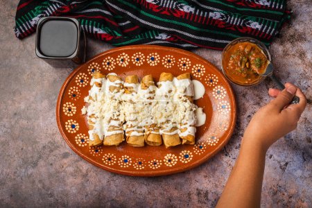 Photo for Woman's hand spooning salsa on a plate of golden potato tacos. Mexican food. - Royalty Free Image