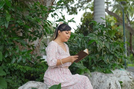 Téléchargez les photos : Femme assise à côté d'un tronc d'arbre dans un parc lisant un livre. Journée mondiale du livre. Concept de lecture. - en image libre de droit