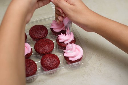 Woman's hands decorating cupcakes with cream cheese frosting.