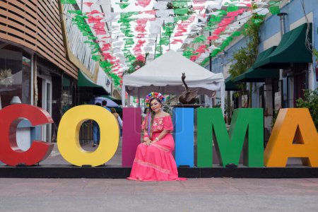 Mujer mexicana vestida con traje tradicional junto a las gigantescas letras de la ciudad de Colima. Celebración del Cinco de Mayo.