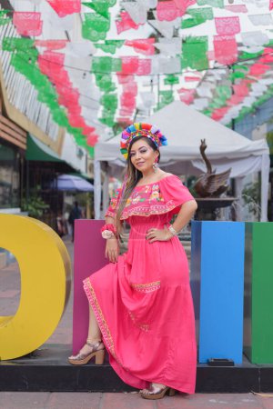Mexican woman wearing traditional costume next to the giant letters of the city of Colima. Cinco de Mayo celebration.