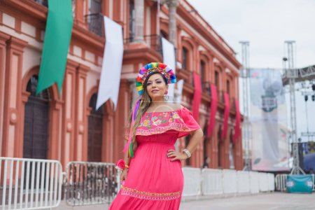 Mexican woman wearing traditional dress. Street decorated with colors of the Mexican flag. Cinco de Mayo celebration.
