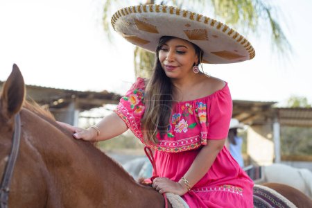 Photo for Mexican woman wearing traditional dress and charro hat on horseback. Cinco de Mayo celebration. - Royalty Free Image