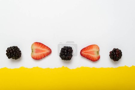 Mûres et fraises coupées sur fond jaune avec bordure en papier blanc déchiré. Contexte d'été.