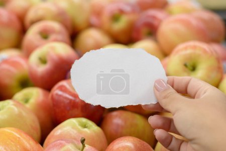Main féminine tenant un morceau de papier déchiré devant une étagère avec des pommes. Liste d'achats concept.