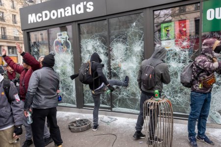 Foto de París, Francia - 23 de marzo de 2023: Manifestante francés rompe la ventana de un restaurante McDonald 's, símbolo del capitalismo global y la dominación cultural estadounidense para activistas de extrema izquierda durante una protesta - Imagen libre de derechos