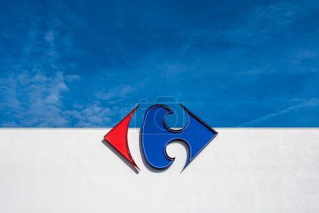 Téléchargez les photos : Anglet, France - 26 avril 2023 : Logo du groupe Carrefour sur un mur blanc et fond bleu ciel - en image libre de droit