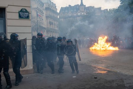 Foto de París, Francia - 1 de mayo de 2023: La policía antidisturbios francesa (CRS) se retira momentáneamente mientras muchos manifestantes incendian los muebles urbanos al final de una protesta contra la reforma de la jubilación en París, Francia - Imagen libre de derechos