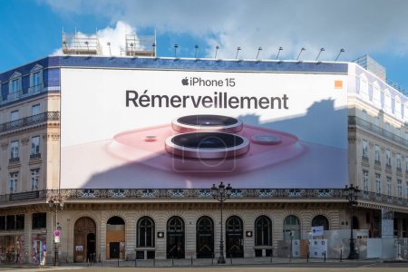 Foto de París, Francia - 6 de diciembre de 2023: Cartel publicitario gigante de Apple iPhone 15 escrito en francés que cubre los andamios de restauración en la fachada de un edificio parisino que alberga una tienda Apple - Imagen libre de derechos