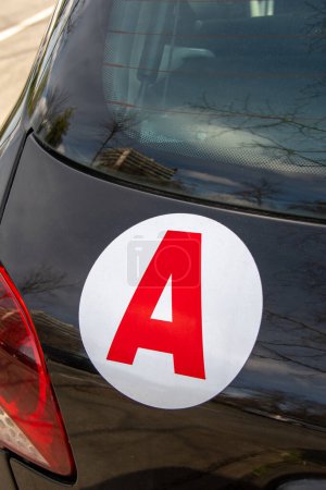 Eine Aufkleberscheibe (für Lehrlinge) auf der Rückseite eines Autos, die in Frankreich darauf hinweist, dass das Fahrzeug von einem jungen Fahrer gefahren wird, der den Regeln des französischen Führerscheins auf Probe unterliegt