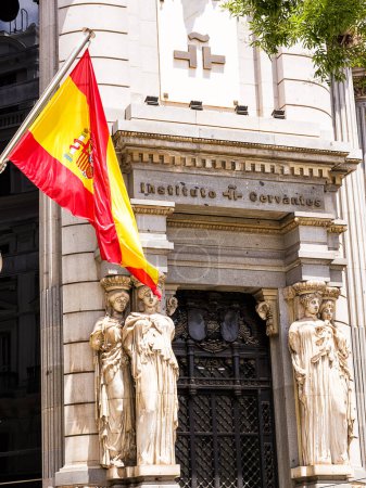 Téléchargez les photos : Madrid, Espagne - 20 juin 2022 : Drapeau espagnol au premier plan et entrée du siège de Madrid de l'Institut Cervantes, un institut qui diffuse la langue espagnole dans le monde. - en image libre de droit