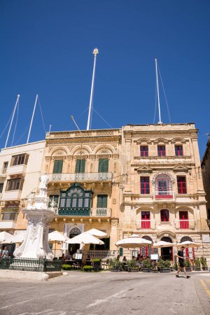 Foto de Vittoriosa, Malta - 17 de junio de 2023: Paraguas con mesas de bar en la plaza de Vittoriosa bajo los edificios - Imagen libre de derechos