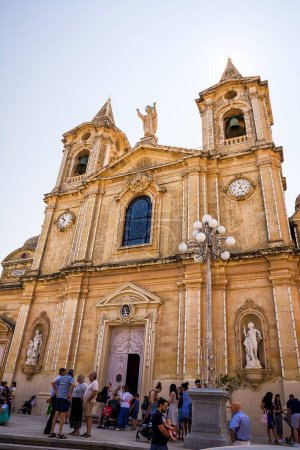 Foto de Zurrieq, Malta - 18 de junio de 2023: Fachada de la iglesia parroquial de Santa Catalina en el pueblo de Zurrieq con fieles después de la misa - Imagen libre de derechos