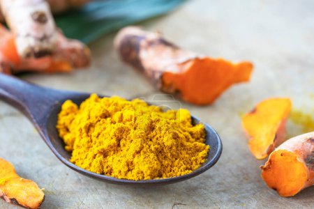 Turmeric powder in black wooden spoon and fresh turmeric (Curcuma longa L) on wooden table with blurred background.