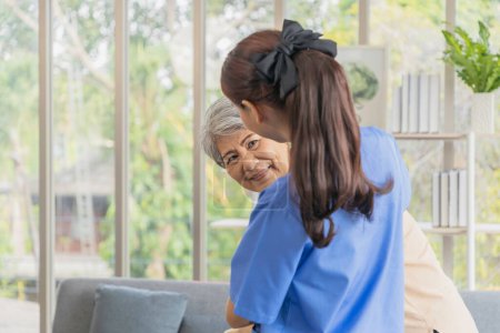 Photo for Asian retired mother receiving health care with her daughter wearing blue nursing clothes at home. - Royalty Free Image