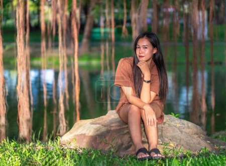 Photo for Portrait of young attractive woman relaxing and sitting on stone in city park with blurred background. - Royalty Free Image