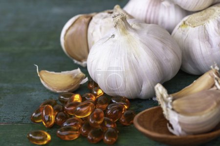 Photo for Garlic bulbs, capsules of oil extract, garlic cloves on wooden spoon, and on old green wooden background, Garlic can help reduce the risk of many diseases. Classified as healthy food - Royalty Free Image