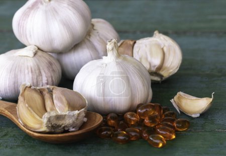 Photo for Garlic bulbs, capsules of oil extract, garlic cloves on wooden spoon, and on old green wooden background, Garlic can help reduce the risk of many diseases. Classified as healthy food. - Royalty Free Image
