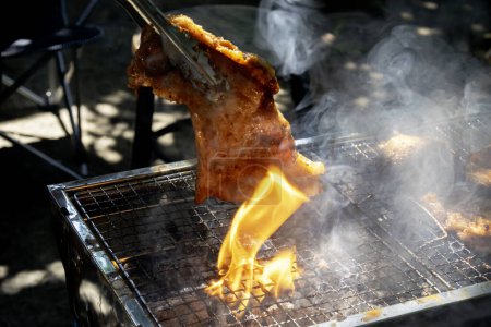 Raw meat in red color is grilled charcoals as local style with dark background. Closed-up roasted pork with fire and smoke. Food, summer, beach and leisure concept. Picnic outdoors, camping. 