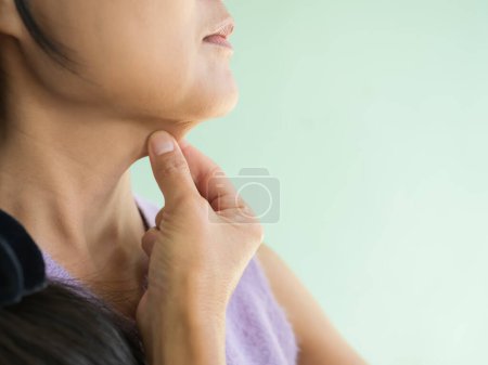 Foto de Women Pinching Layer Fat Under Chin on Green Wall Background,Excess Fat,Sagging Muscles,Saggy Neck Woman Close Up,Overweight Body,for Fitness Health Lifestyle Concept.Authentic Skin Tan Asian. - Imagen libre de derechos