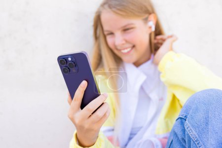 Photo for Teenage girl using mobile phone and listening to music on wireless earbuds - Royalty Free Image