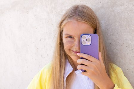 Photo for Teenage girl holding mobile phone's camera in front of her eye - Royalty Free Image