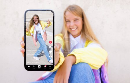 Téléchargez les photos : Adolescente montrant un téléphone mobile avec un échantillon de contenu vidéo partagé sur les médias sociaux - en image libre de droit