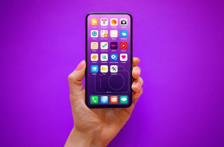 Téléchargez les photos : Téléphone portable à la main sur fond violet avec des icônes d'écran d'accueil échantillon sur l'écran - en image libre de droit