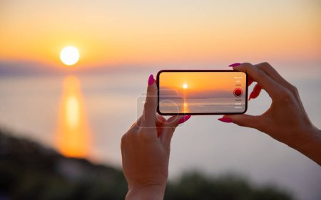 Photo for Woman holding mobile phone in hands and taking sunrise photo - Royalty Free Image