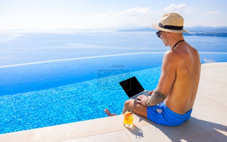 Photo for Man working with laptop while sitting by infinity pool with beautiful sea view - Royalty Free Image