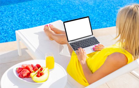 Photo for Woman using laptop by the pool, blank white screen mockup - Royalty Free Image