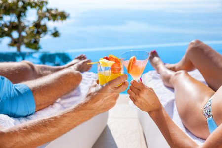 Photo for Couple holding cocktail glasses and relaxing by infinity pool with beautiful sea view - Royalty Free Image