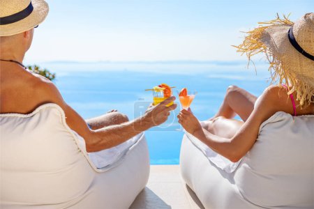Photo for Couple holding cocktails while relaxing by the pool on vacation - Royalty Free Image