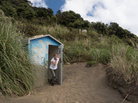 Photo for A lady exits a remote toilet hut in dunes with scarf over her face due to smell. - Royalty Free Image