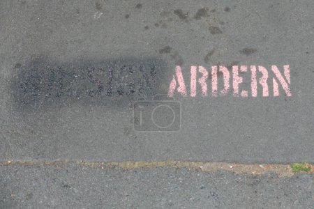 Photo for Stencilled lettering on a New Zealand pavement says 'Ardern'. Rubbed out and just visible also word 'resign'.Political statement slogan.Hashtag - Royalty Free Image