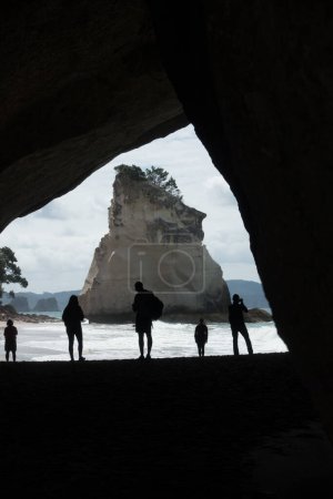 Foto de Una imagen vertical que mira a través de la cala de la catedral hacia la roca de la catedral con los turistas silueta mientras miran el atractivo natural.Nueva Zelanda - Imagen libre de derechos