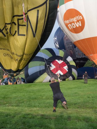 Photo for Bristol-UK-August 11 ,2023 - At Bristol Balloon Fiesta a man can be seen holding a rope tethering a balloon as it is inflated .He is being pulled and dragged struggling to hold on - Royalty Free Image